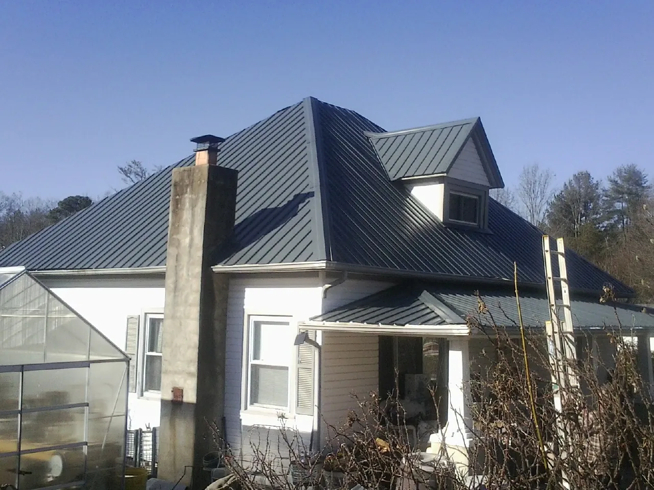 Dark blue standing seam metal roof on a white farmhouse with dormer — Slate & Tile Roof Repair by Roofing Brothers in Texhoma