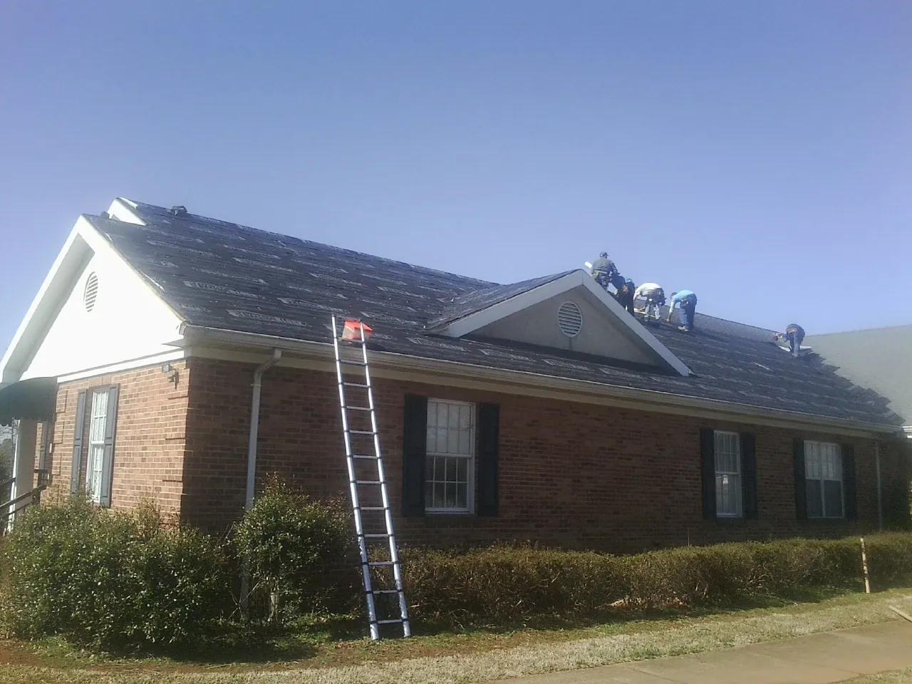 Crew tearing shingles off a brick ranch roof with a ladder set — Metal Roof Repair work by our crew in Texhoma