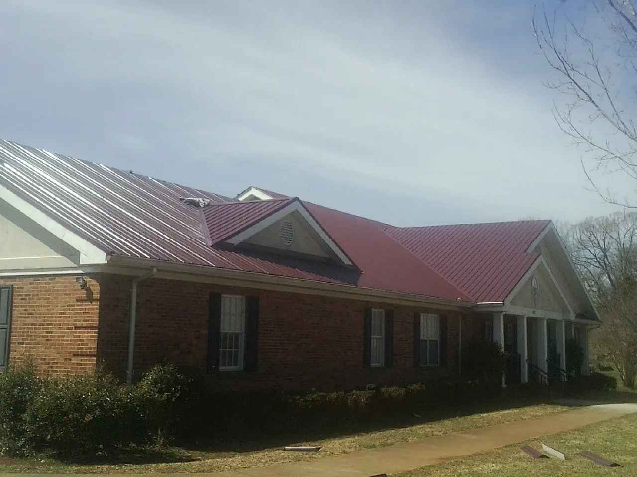 Red metal roof with gabled entries on a long brick building, from a Hail Damage Roof Repair job in Texhoma