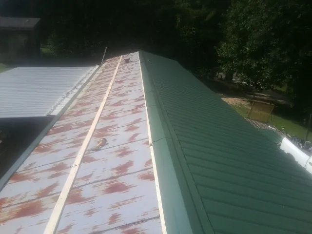 Old rusted panels beside newly installed green metal roofing — Wind Damage Roof Repair by Roofing Brothers in Texhoma