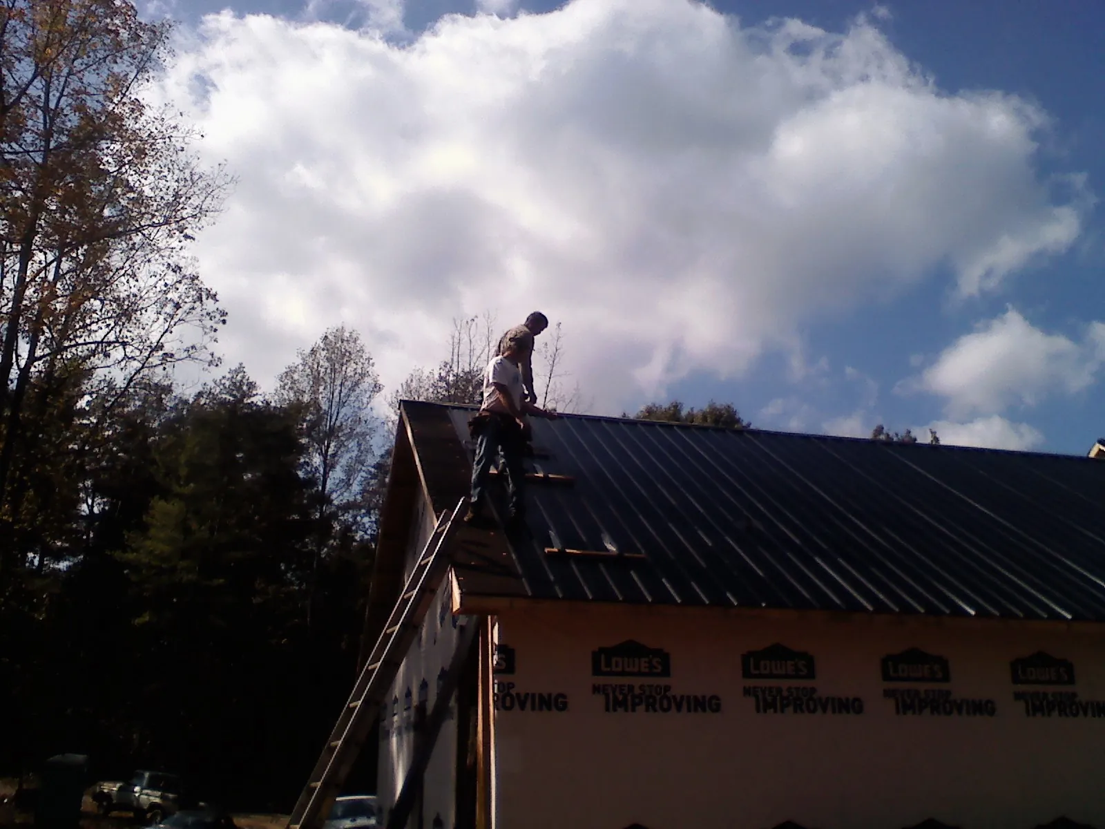 Roofer fastening dark metal panels high against a cloudy sky, from a Roof Inspection job in Texhoma