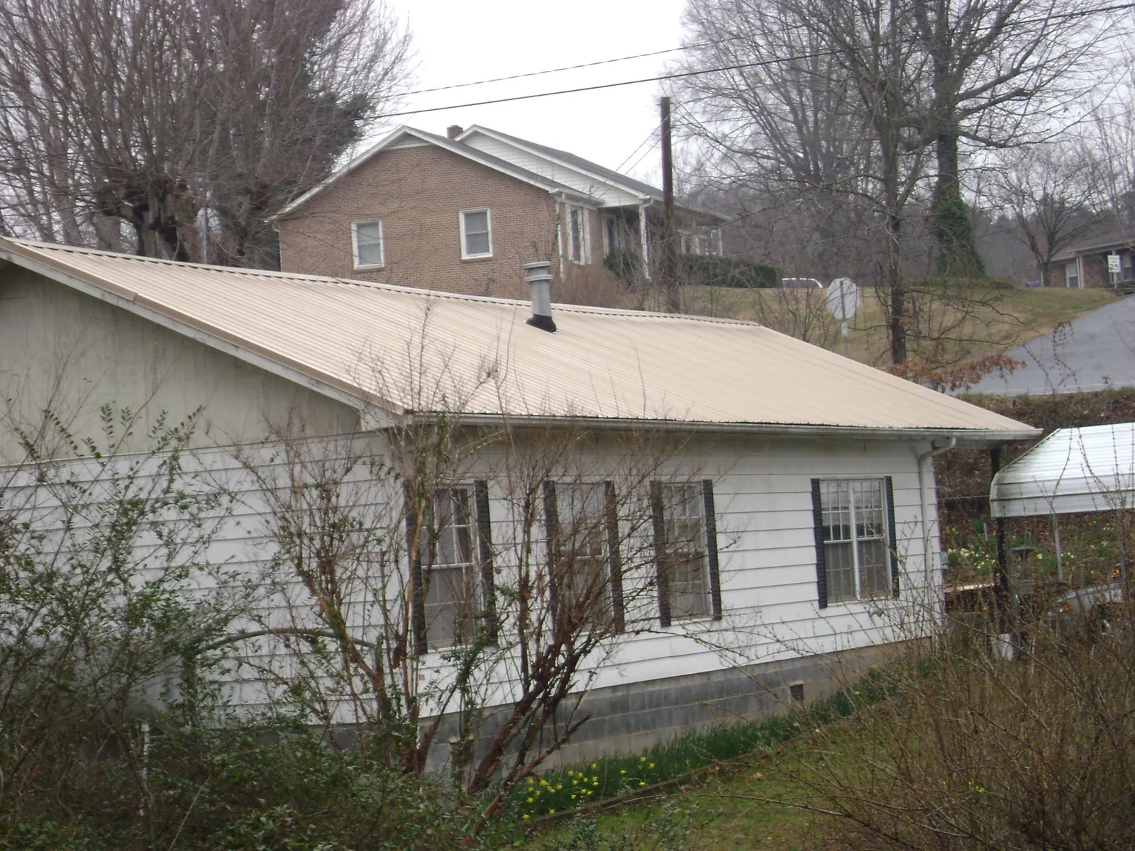 Tan metal roof on a white sided house set into a hillside — Commercial Roofing by Roofing Brothers in Texhoma