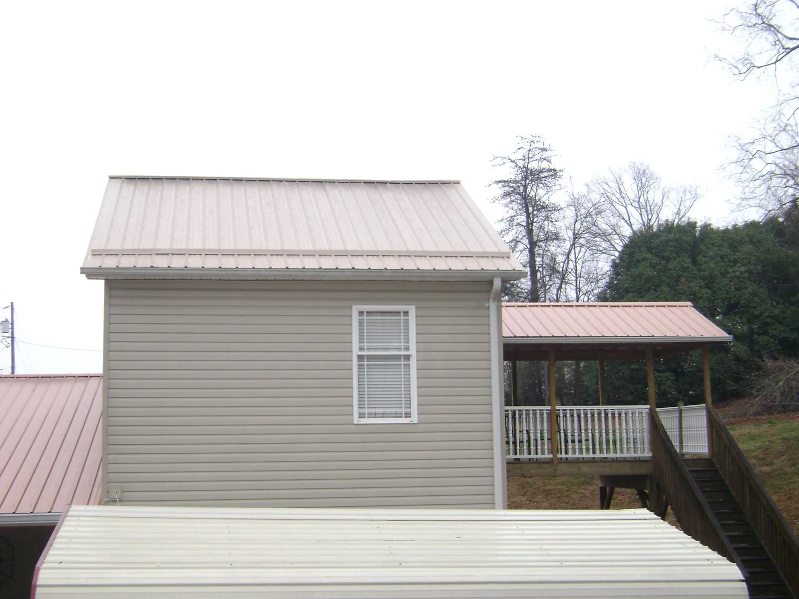 Tan metal roofs on a two story addition and attached porch, from a Roof Replacement job in Texhoma